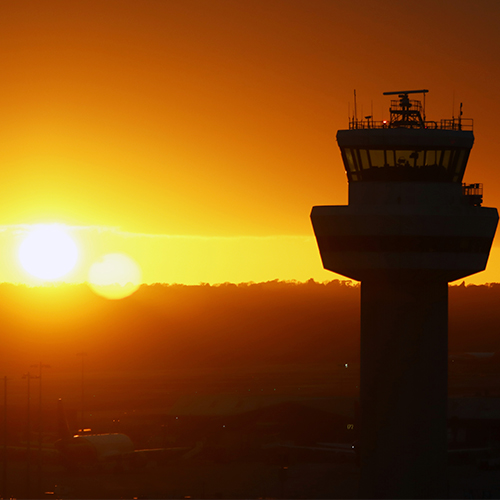 a photograph of the London Gatwick control tower silhouetted against a rich orange sunset sky