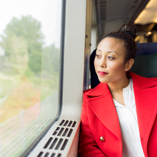 A photograph of a woman looking out of a window at trees and greenery from inside a moving train