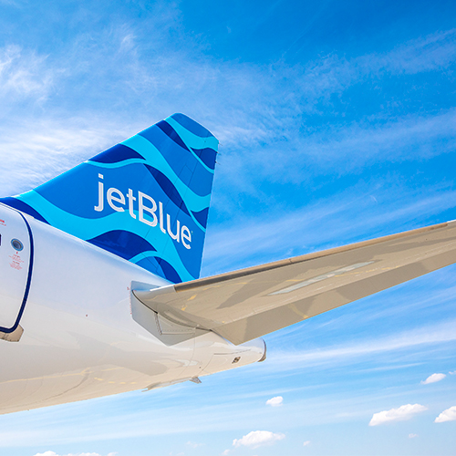 a low angle photo of a JetBlue plane tail fin against a blue sky backdrop